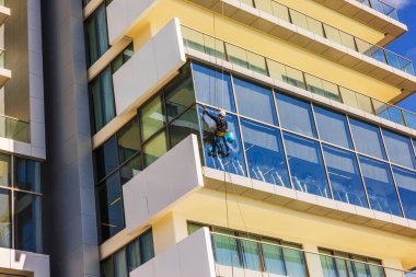 Pencere temizleyicisi, parlak güneş ışığı altında modern gökdelenlerin cam cephelerini temizlerken asılmış. Meksika mı? Cancun..
