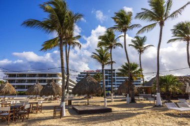 Palapas ve Corendon Oteli 'nin arka planında, kumlu sahilde palmiye ağaçları. Parlak mavi gökyüzünün altında dağınık bulutlar..