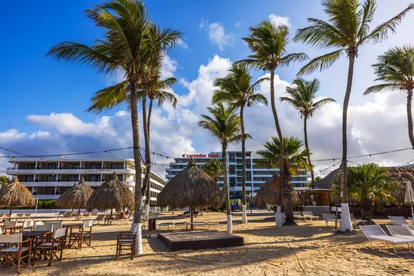 Palapas ve Corendon Oteli 'nin arka planında, kumlu sahilde palmiye ağaçları. Parlak mavi gökyüzünün altında dağınık bulutlar..