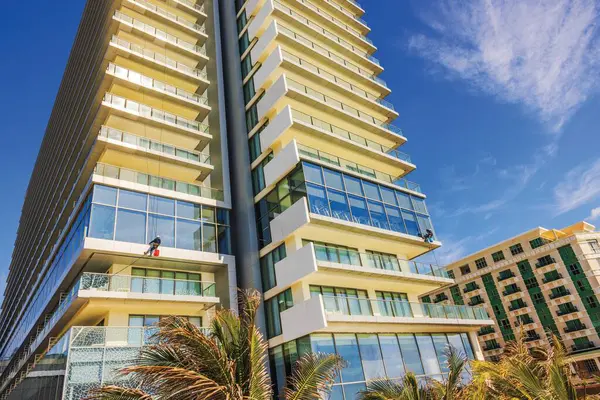 Açık mavi gökyüzü altında çalışan cam temizleyicileri olan yüksek katlı bir otel binası. Meksika mı? Cancun.. 