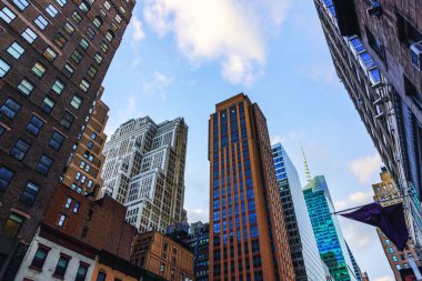 Mavi gökyüzü ve bulutlara karşı farklı mimari tarzlara sahip New York gökdelenlerine bakıyorum..