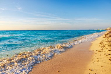 Cancun, Meksika 'daki Karayip kıyıları boyunca kumlu sahil ve turkuaz dalgaların altın saat manzarası.
