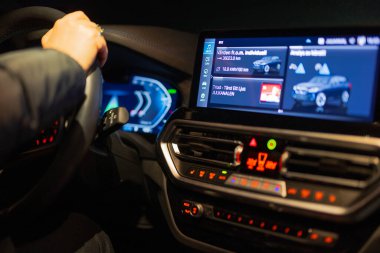 Aydınlatılmış araba gösterge paneli ve navigasyon ve ortam kontrollerini gösteren bilgi ekranı ile el ele tutuşan direksiyon. 