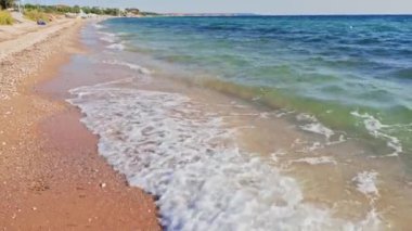 Dalgalar yaz atmosferinde canlı Ege Denizi ile güneşli Halkidiki kıyı şeridinde kumlu çakıl taşlarını nazikçe sürüklüyor..