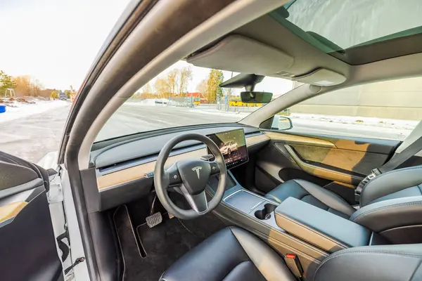 Tesla Model Y 'nin iç mekan gösteriminin açık kapı görünümü, gösterişli gösterge paneli, dokunmatik ekran ve panoramik çatı güneş ışığı altında. 