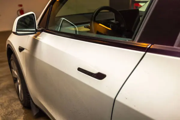 Tesla Model Y yakın çekim vitrin parlak kapı kolu ve kapalı otoparkta modern yan ayna tasarımı. 