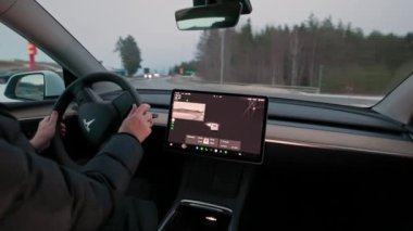 Tesla Modeli Y 'den dönme dolambaçlı kavşağa doğru dönen sürücü, dönüş sinyali etkinleştirildi ve merkezi dokunmatik ekranda trafik görüntüsü gösteriliyor. 