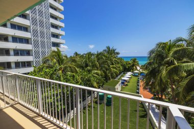 Yeşil palmiye ağaçlarına bakan otel balkonundan manzara. Tropik tatil köyü bahçesi ve Atlantik Okyanusu. Miami Beach, ABD.