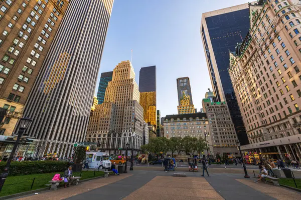 İnsanlar banklarda dinleniyor ve yüksek gökdelenlerle Central Park yakınlarında yürüyorlar. - New York. ABD. 