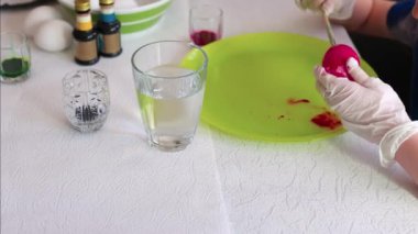 Çocuk kırmızı Paskalya yumurtasını yeşil tabakta fırçayla boyuyor, etrafı su ve boya şişeleriyle çevrili. İsveç.