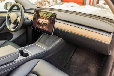 Tesla Model Y iç tasarımı minimalist gösterge paneli, dokunmatik ekran, siyah deri koltuklar ve kışın ahşap süsleme.