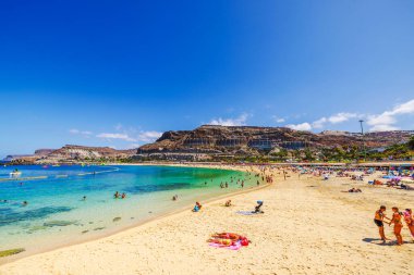 Atlantik Okyanusu 'nun turkuaz sularıyla kayalık uçurumlara inşa edilmiş otellerle kumlu sahillerin tadını çıkaran turistler. Gran Kanaryası, Las Palmas, İspanya. 