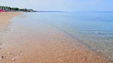 Küçük çakıl taşları ve hafif dalgalarıyla kumsal Ege Denizi 'nde kıyıya vuran güneş panjurları ve şemsiyelerle kaplı. Halkidiki, Yunanistan. 