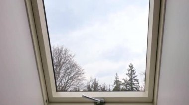 Beyaz çerçeveli, bulutlu gökyüzünü ve dışarıdaki çıplak ağaçları gösteren villa odasındaki yatakhane penceresi kameralar yavaşça yaklaşırken. İsveç.