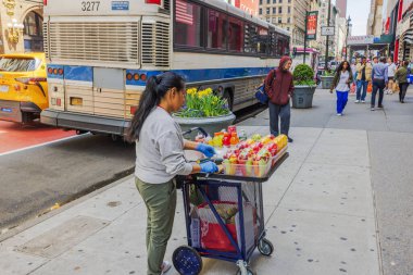 New York 'ta park halindeki otobüsün yanındaki kaldırımda taze meyve tabakları ve içecekler satan bir sokak satıcısı. - New York. ABD. 