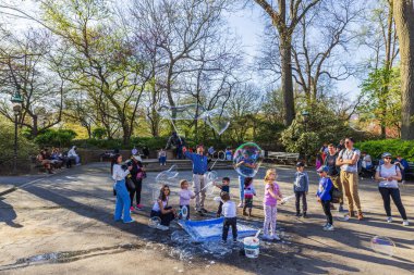 Çocuklar güneşli bahar gününde şehir parkında dev sabun köpüğüyle oynuyorlar. - New York. ABD. 