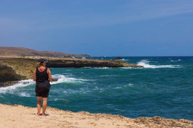 Aruba 'daki Arikok Ulusal Parkı' nın kayalık kıyılarında duran bir kadın Karayip Denizi 'nin engebeli kıyı şeridine çarpan dalgaları seyrediyor..