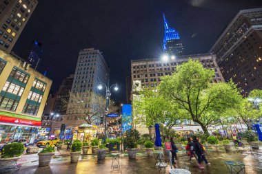 Gece Herald Meydanı 'ndaki şehir ışıklarını yansıtan ıslak kaldırım yeşil ağaçlar, sokak lambaları ve parlayan Empire State Binası. - New York. ABD. 