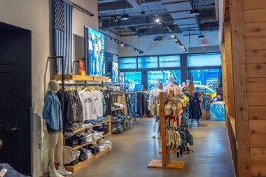 Parlak ışık altında sergilenen kot ceketli, tişörtlü ve aksesuarlı modern giyim mağazası. - New York. ABD.