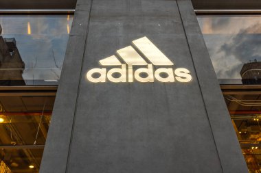 Aydınlatılmış Adidas logosunun kentsel çevrenin cam yansımalarıyla modern beton mağaza vitrinine yakın görüntüsü. - New York. ABD. 