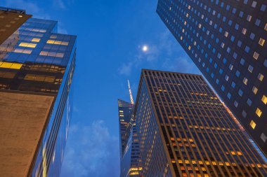 New York 'ta alacakaranlıkta aydınlık gökdelenlerin parlayan ofis pencereleri ve derin mavi gökyüzü. 