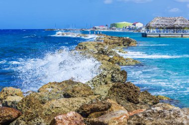 Dalgalar, turkuaz Karayip Denizi 'nde kıyı şeridi oteli ve sazdan restoranı olan kayalık dalgalara çarpıyor. Curacao.