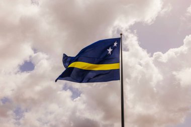 Curacao bayrağı dalgalanır bulutlu gökyüzünde bayrak direğinde.