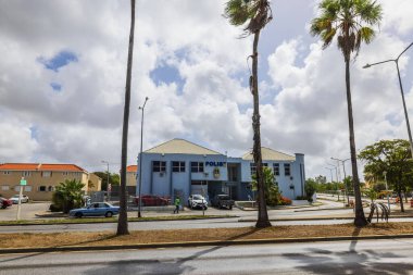 Mavi cepheli karakol binası, park halindeki arabalar, palmiye ağaçları ve tropik şehir ortamında bulutlu gökyüzü.. 