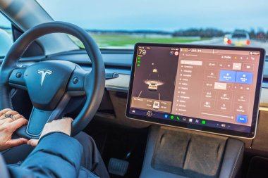 Dokunmatik ekranda otomatik pilot ve kontrol ayarları kullanırken direksiyon tutan Tesla Model Y sürücüsünün görüntüsünü kapat. 