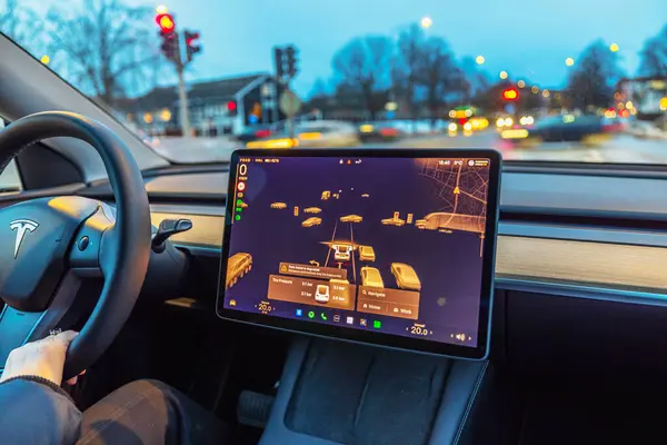 Tesla Model 3 'ün yakın görüntüsü otomatik pilot görüntüsü dokunmatik ekranda, sürücü direksiyonu tutarken. İsveç. 