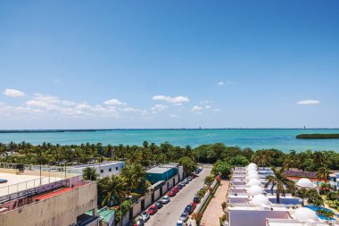 Turkuaz Karayip Denizi manzarası. Palmiye ağaçları, binalar ve açık mavi gökyüzünün altında park edilmiş arabalar. Meksika mı? Cancun..