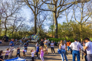 Central Park Manhattan 'da bahar gününün tadını çıkaran insanlar, uzun ağaçların arasında dev sabun baloncuklarıyla oynayan çocuklar. - New York. ABD.