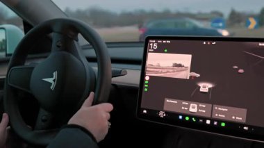 Otomatik pilot sistemi gerçek zamanlı yol verilerini gösterirken, Tesla Model 3 'ü kullanan kadın ellerini direksiyonda tutuyor. 