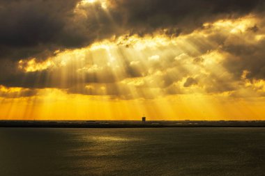 Karayipler 'in sakin denizi üzerinde ağır bulutların arasından yükselen dramatik altın güneş ışığı suya ve uzak ufka ışıldayan ışınlar saçıyor. Meksika mı? Cancun..