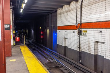 New York 'taki Rockefeller Center istasyonundaki metro platformunda raylar, tünel girişi ve uyarı levhaları var. - New York. ABD. 
