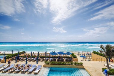 Güneşli bir tatil gününde, mavi gökyüzünün altında havuz, güneş pansiyonları ve şemsiyelerle Karayip Denizi manzarası. Cancun. Meksika.