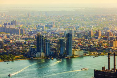 New York şehrinin yüksek açılı manzarası modern gökdelenler, East River ve su üstünde dalgalanmalar bırakan tekneler. ABD.