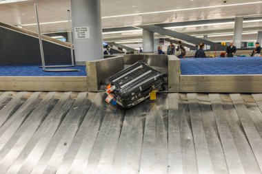 Havaalanında bagaj etiketli siyah bavul, taşıyıcıdan bagaj teslim bandına, bekleyen yolcularla birlikte hareket ediyor. - New York. ABD.