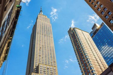 Empire State Binası 'nın alçak açılı görüntüsü beyaz bulutlu mavi gökyüzüne karşı Manhattan üzerinde yükseliyor. - New York. ABD.