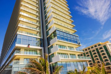 İşçiler, mavi gökyüzünün altında balkonları ve palmiye ağaçları olan uzun ve modern otel binasının camlarını temizliyorlar. Meksika mı? Cancun..