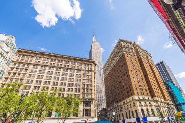 Empire State Binası ve çevresindeki tarihi binalar mavi gökyüzü altında ve 34. Cadde 'de beyaz bulutlar var. - New York. ABD.