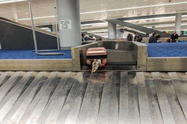 Bagaj kemeriyle havaalanındaki bagaj teslim yerine gelen bavul arka planda yolcularla birlikte. - New York. ABD. 