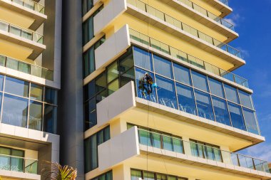 İşçi, Karayip tatil köyünde mavi gökyüzü olan modern otel binasının camlarını temizlerken askıya alınmış. Meksika mı? Cancun.. 