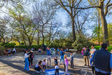 Güneşli bir günde, yetişkin gözetiminde bahar parkında dev sabun köpüğüyle oynayan çocuklar. - New York. ABD. 