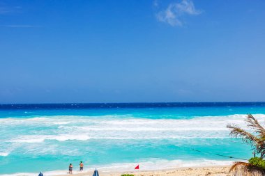 Turistler, turkuaz Karayip Denizi yakınlarındaki kumlu sahil boyunca güçlü dalgalar ve kırmızı uyarı bayrağıyla yürüyorlar. Cancun. Meksika. 