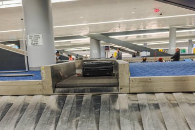Modern havaalanı terminalindeki bagaj atlıkarıncasında bekleyen insanlarla birlikte siyah bavul. - New York. ABD.