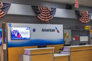 American Airlines 'ın JFK havaalanındaki 12 no' lu girişi, ekranı, masası ve ABD bayraklarıyla. - New York. ABD. 