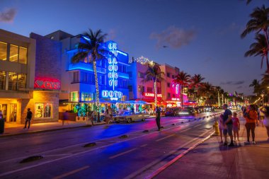 Ocean Drive 'ın neon ışıklı otelleri, palmiye ağaçları, klasik arabalar ve Florida' da yürüyen turistlerle akşam manzarası. Miami Plajı. ABD.