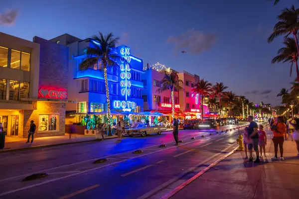 Ocean Drive 'ın neon ışıklı otelleri, palmiye ağaçları, klasik arabalar ve Florida' da yürüyen turistlerle akşam manzarası. Miami Plajı. ABD.