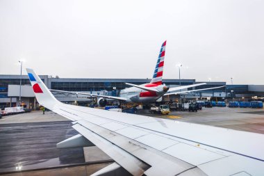 Terminaldeki American Airlines uçağında kargo yükleme ve yer araçları yakındaki uçak penceresinden görüldü. - New York. ABD. 
